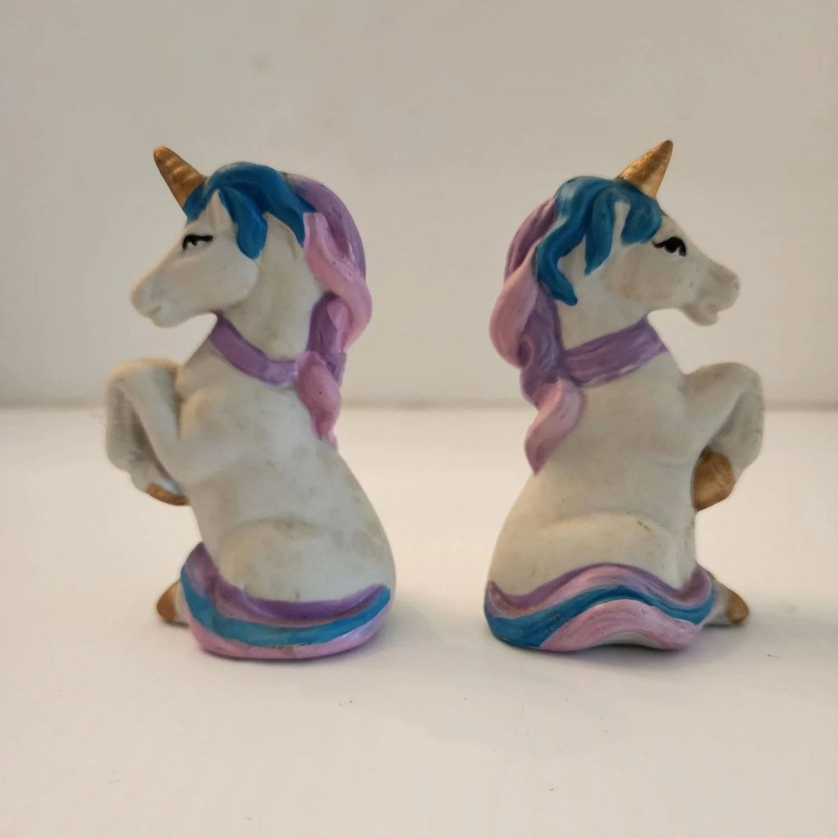 Two ceramic unicorn figurines sitting on a table, one white and one pink, with intricate details and a glossy finish.