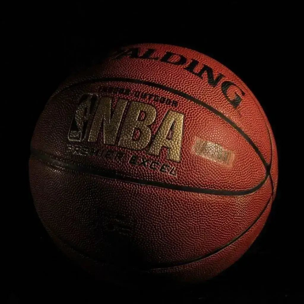 In a shadowy room, a basketball stands out, its vibrant texture contrasting with the surrounding darkness.